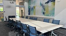 12 rolling chairs at board table with green, blue, and white mural on wall behind
