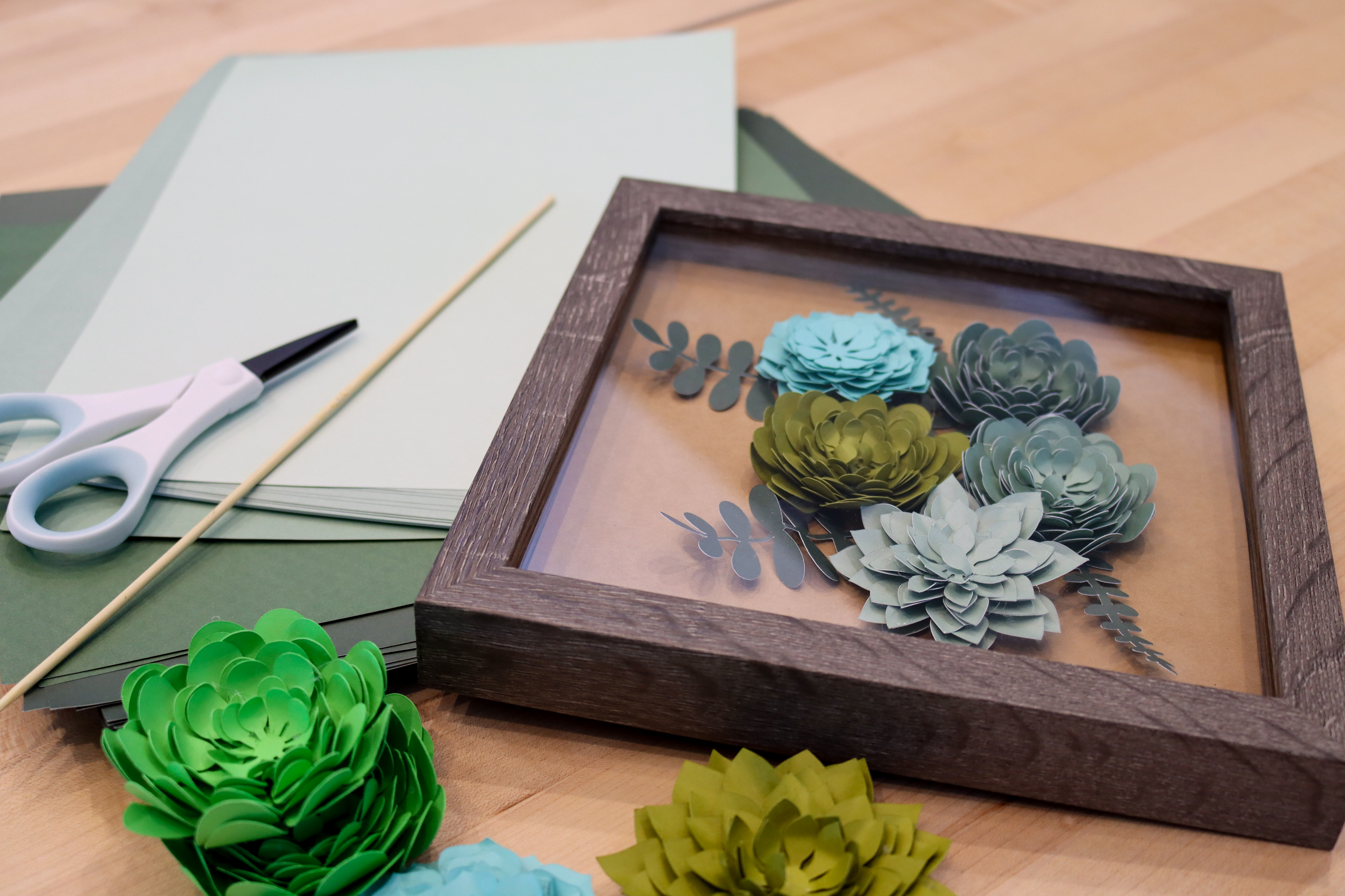 A shadow box that has paper eucalyptus flowers inside.
