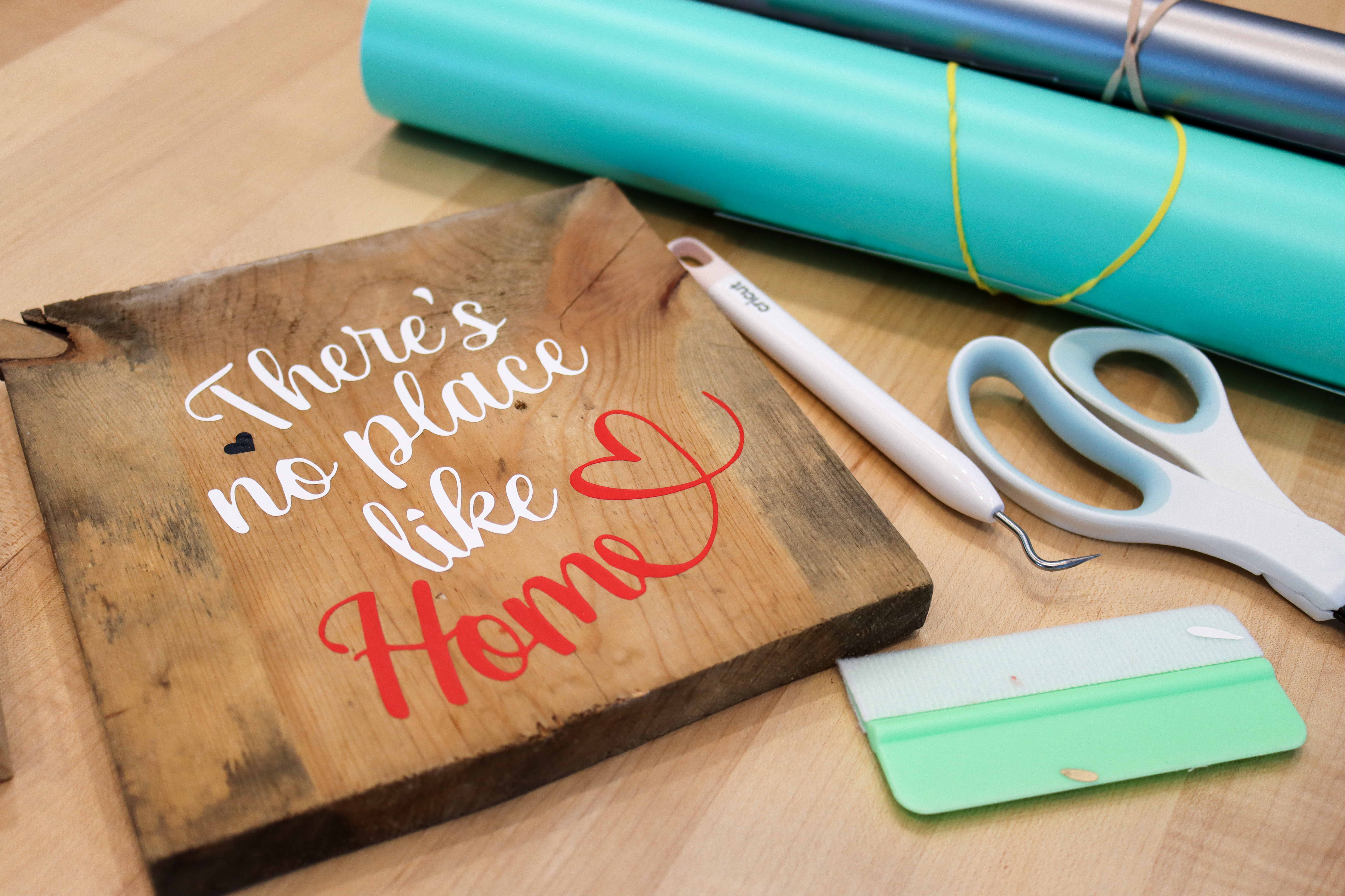 A square wooden sign that says There's No Place Like Home in curvy script vinyl