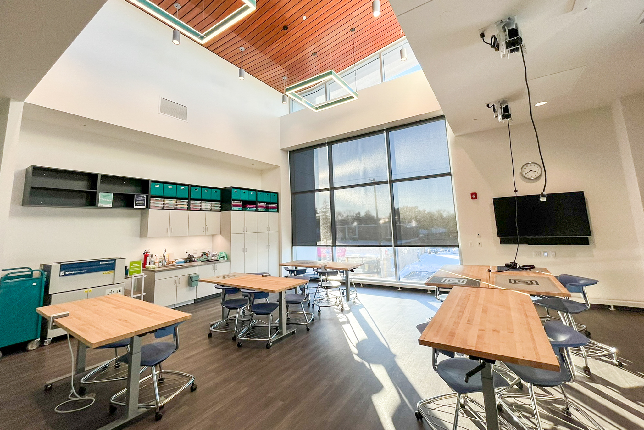 Studio space with large windows and natural light, gray floors, wooden tables and lofted ceiling with wood panelling.