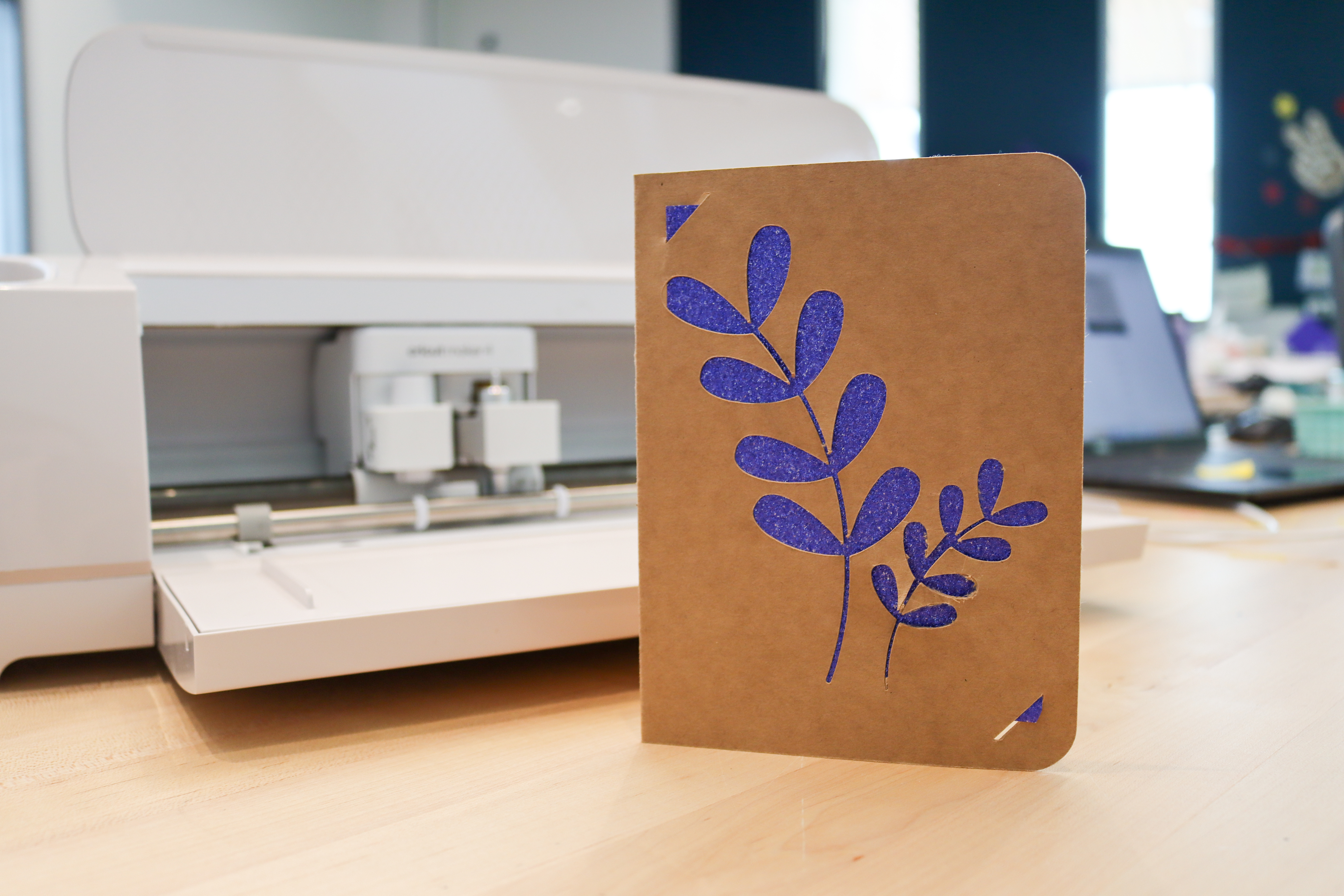 Brown paper greeting card with a cutout of a leaf sprig, with sparkly blue paper inserted behind the cutout.