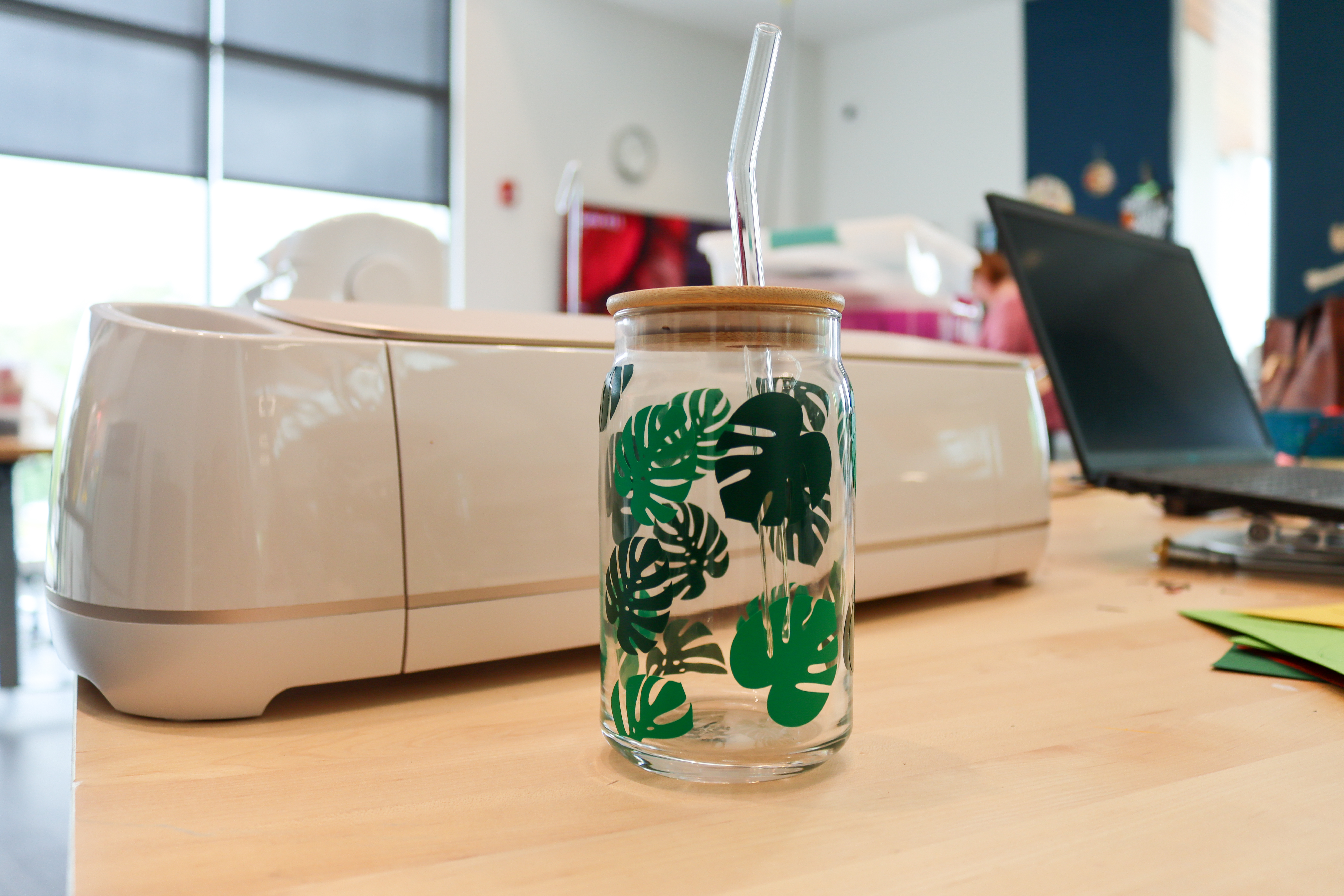 Clear glass cup decorated with palm fronds in shades of green, with a lid and straw.