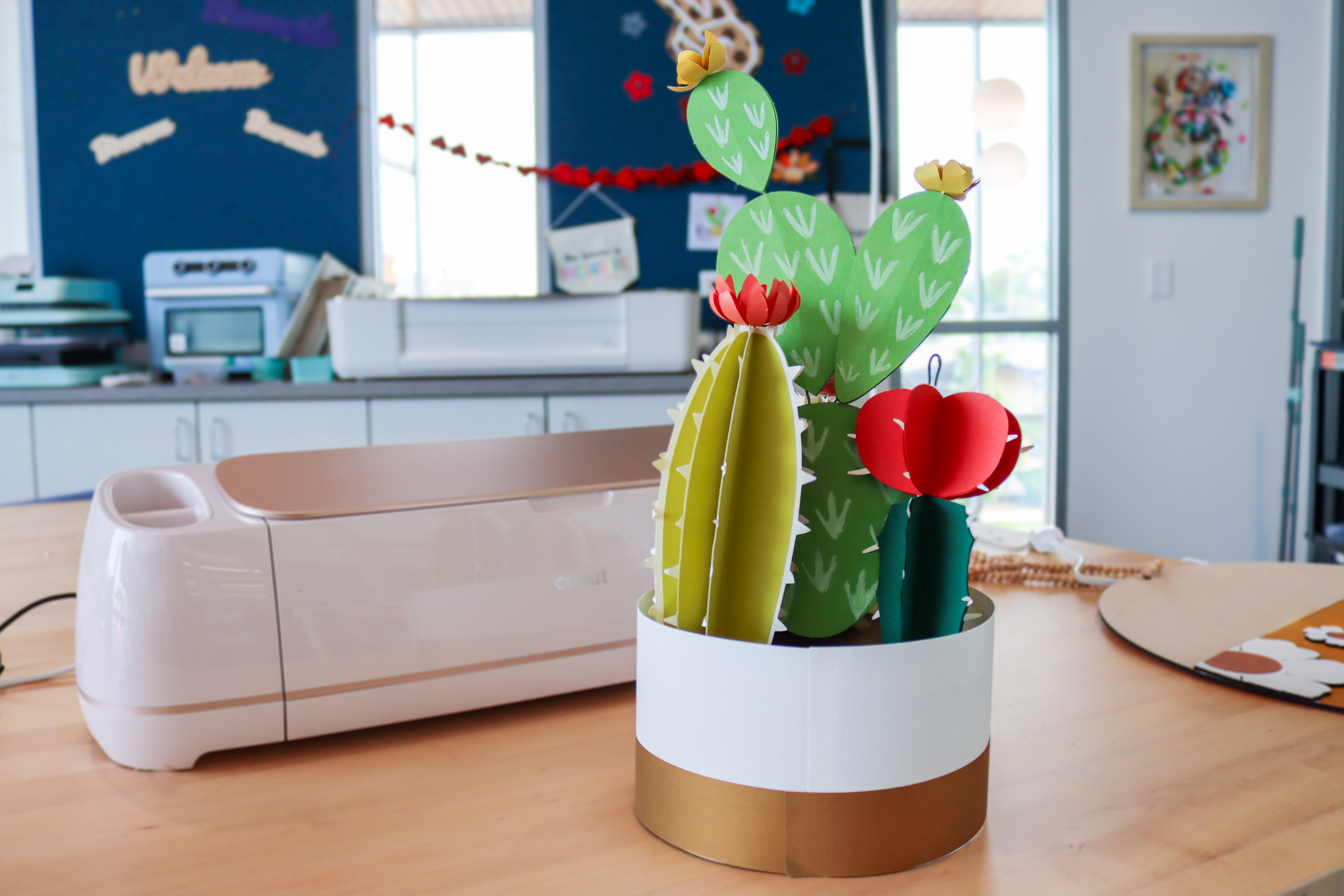 White paper pot with three different cacti made of paper in different shades of green with red and yellow flowers on top