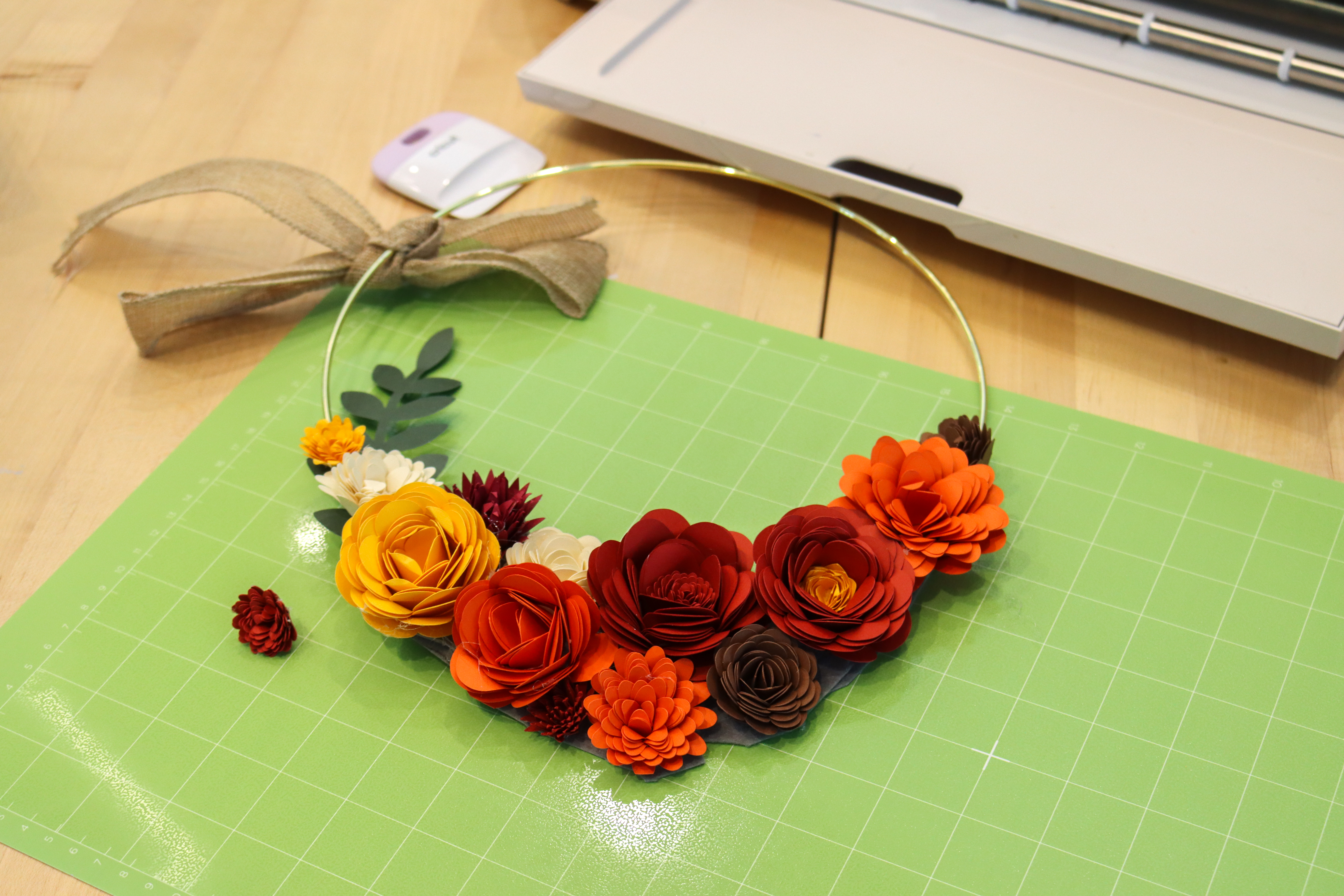 Metal wire wreath with paper flowers filling the bottom half in shades of red, orange, and yellow.