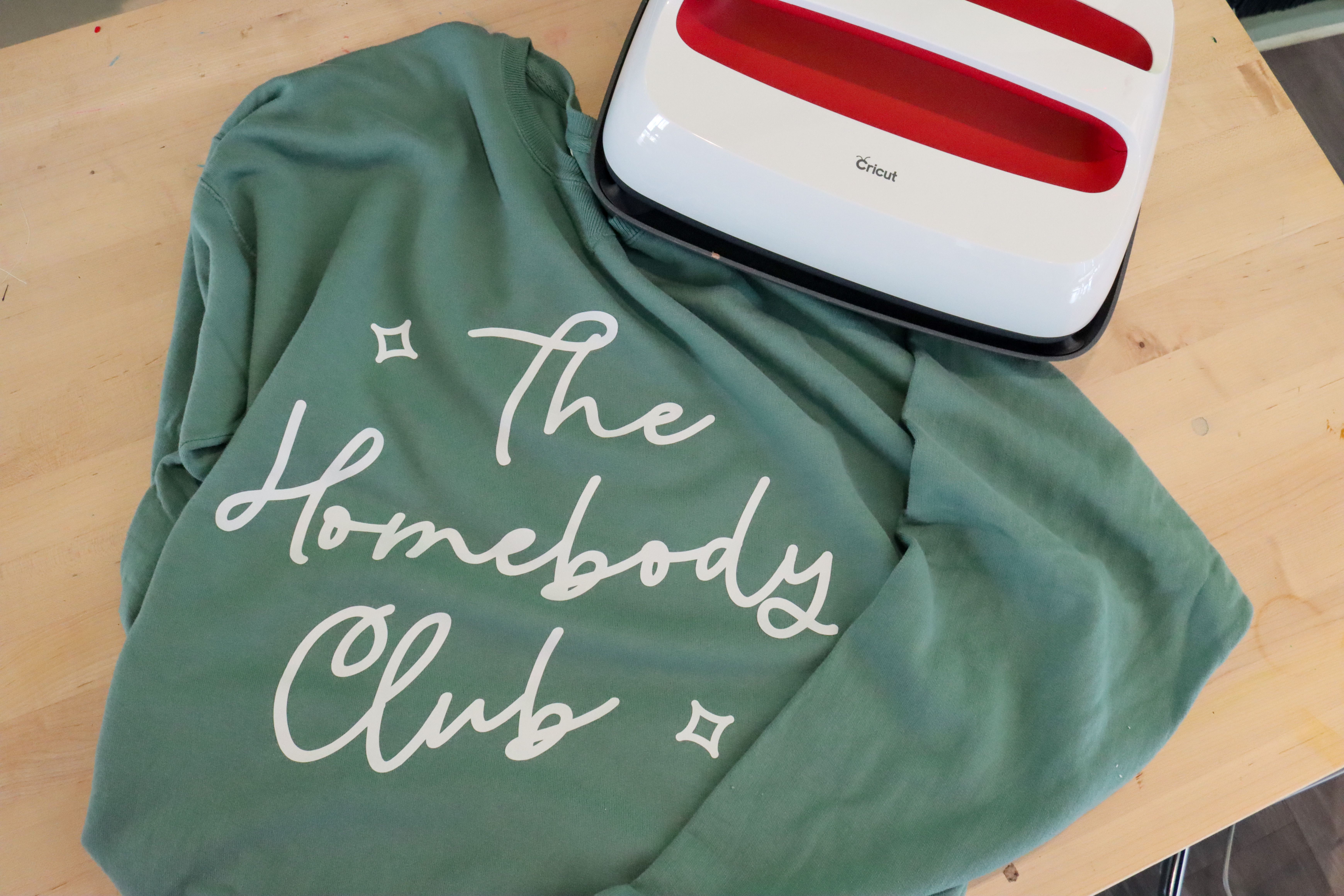 Sage green sweatshirt with white script text that says the homebody club.
