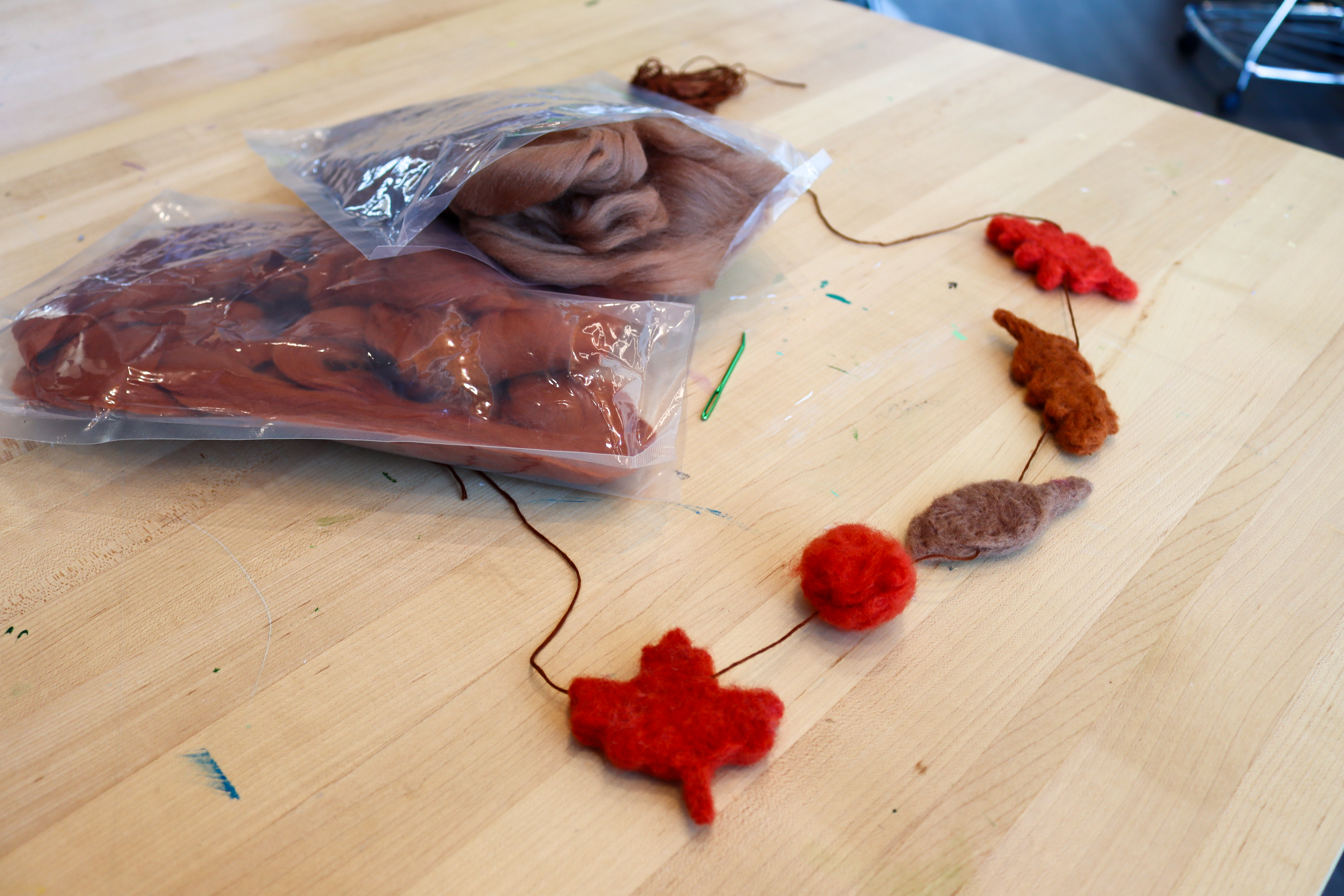 Wool felted garland in the shape of various leaves in shades of red and brown.