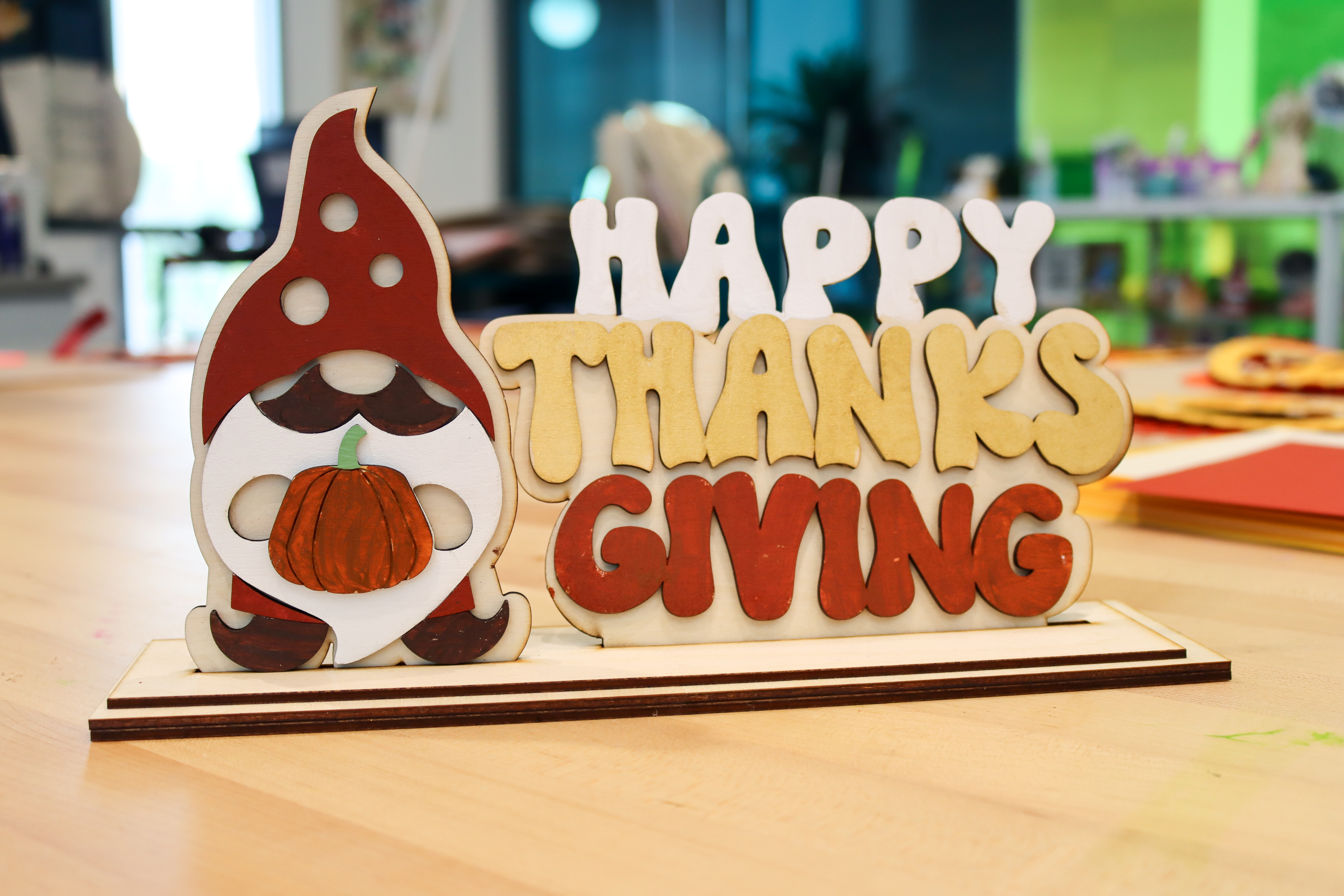Wooden stand decor with bubbly letters that says Happy Thanksgiving next to a gnome holding a pumpkin.