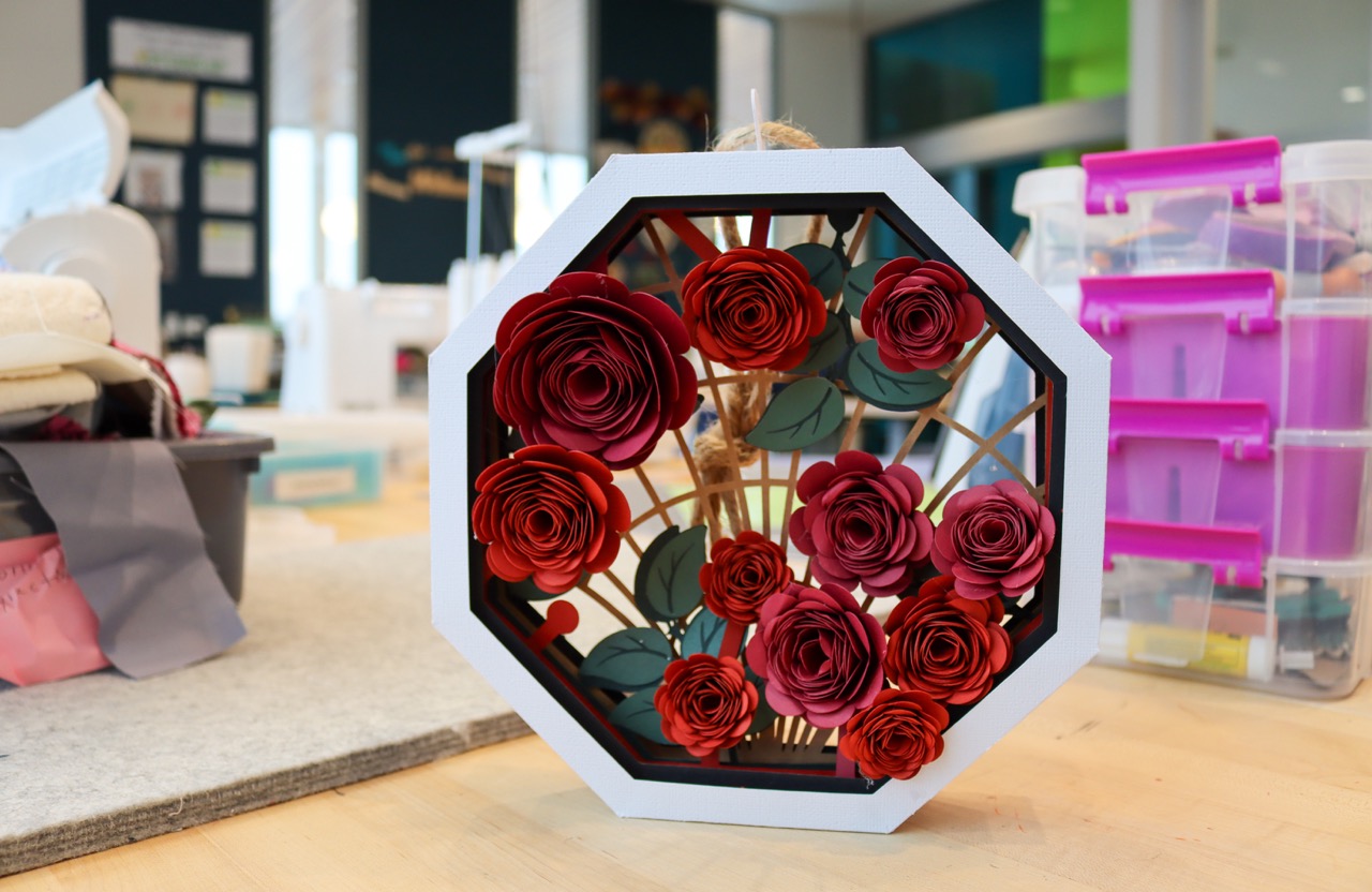 Octagonal paper shadow box with red paper roses inside growing on a lattice.