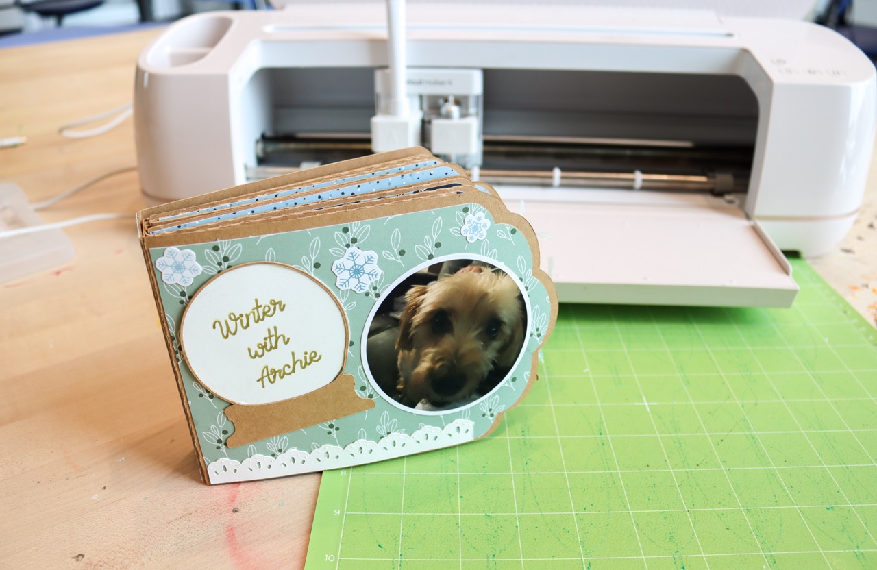 Small scrapbook with a photo of a dog next to a snow globe that says Winter with Archie on the cover.