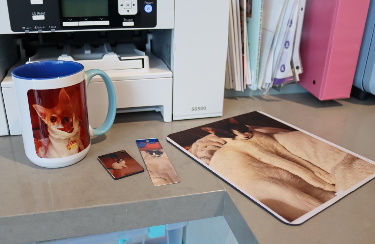 Samples of a mug, keychain, bookmark, and mousepad with photos of pets printed on them using sublimation.