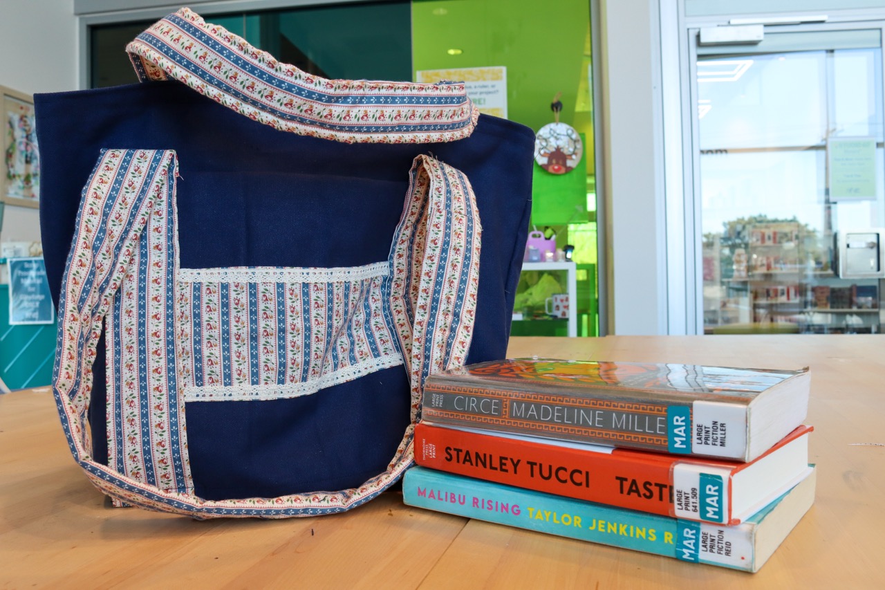 Navy blue tote bag with floral-patterned handles next to a stack of books.